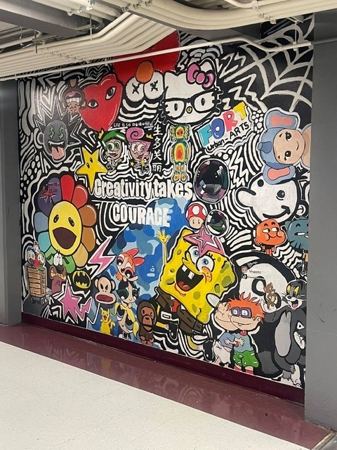 Colorful graffiti mural with cartoon characters and the phrase "Creativity takes Courage" on a school hallway wall.